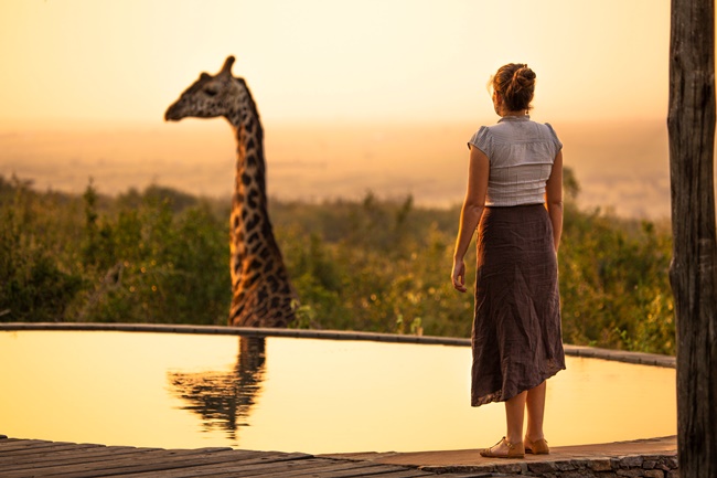 Frau steht einer Giraffe gegenüber im rötlichen Abendlicht