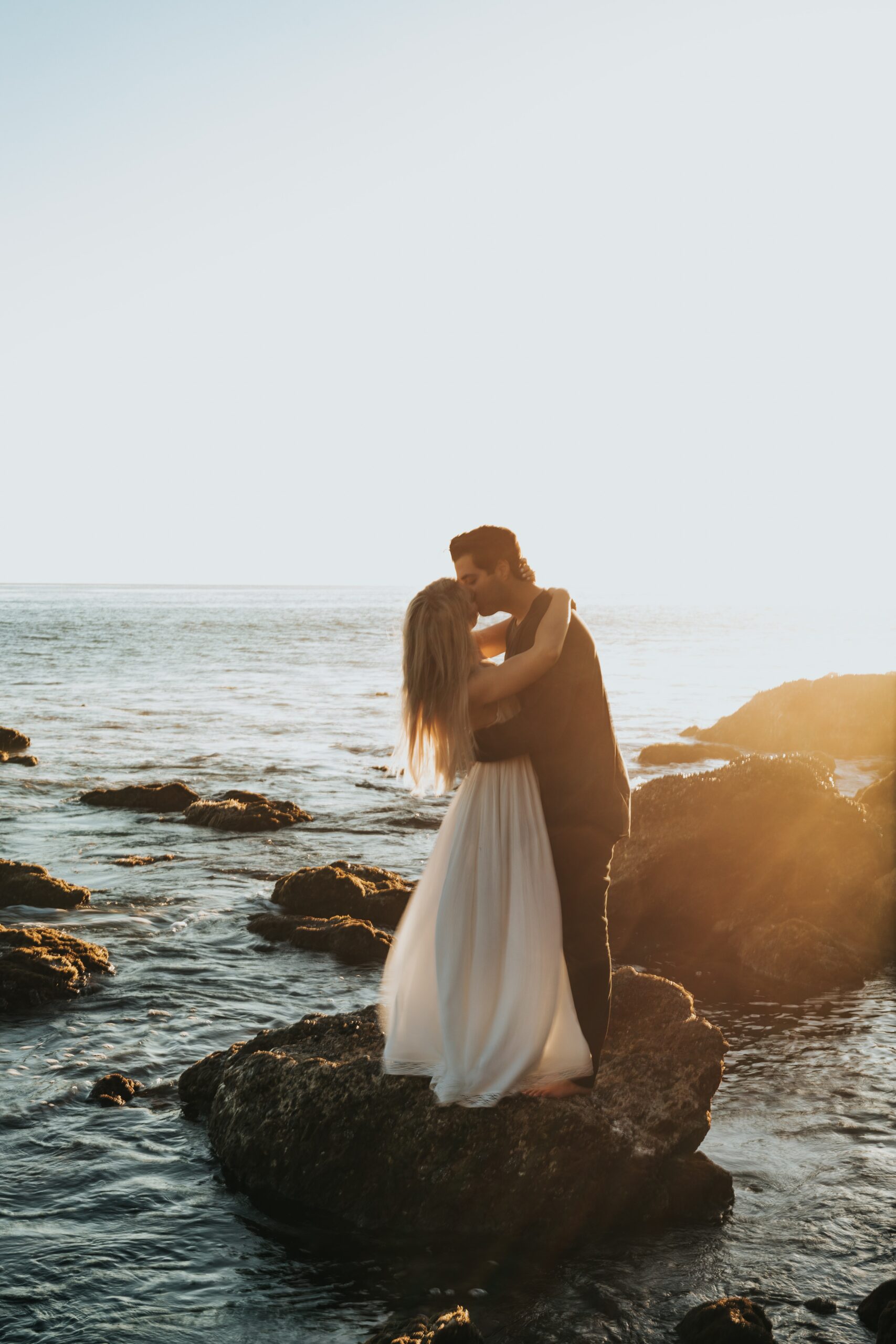 Brautpaar küsst sich auf meerumspülten Felsen