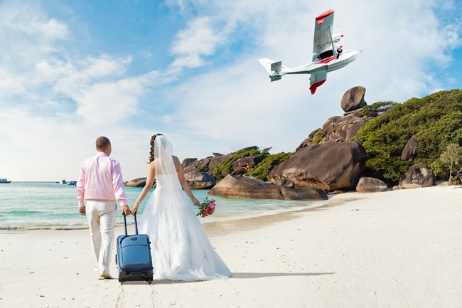 Glückliches, neu verheiratetes Ehepaar in ihren Flitterwochen an einem sonnigen Strand in Thailand, im Hintergrund ein Flieger