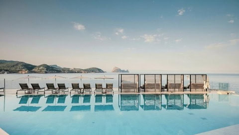 Infinity-Pool mit Blick auf das Meer und die Insel Es Vedrà, eingerahmt von modernen Sonnenliegen im 7Pines Resort Ibiza