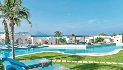 Poollandschaft mit weißen Villen, Palmen und Sonnenliegen in mediterraner Gartenanlage des 7Pines Resort Ibiza