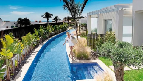 Frau im Sommerkleid spaziert am privaten Pool entlang – tropisch bepflanzter Villenbereich im 7Pines Resort Ibiza