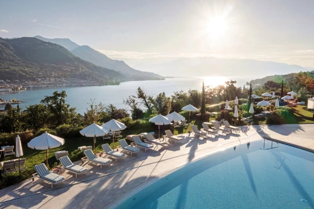 Sonniger Poolbereich im A-ROSA Gardasee Salò mit Liegen, weißen Sonnenschirmen und weitem Blick auf den Gardasee