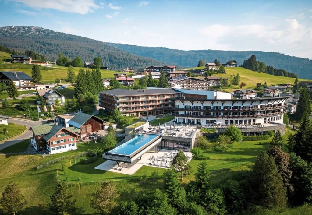 Außenansicht des A-ROSA Ifen Hotels im Kleinwalsertal mit Pool, Wiesen und Berglandschaft