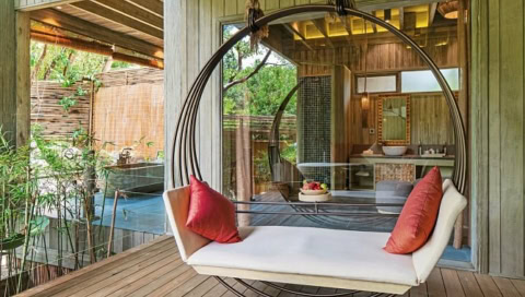 Runde Hängeliege mit roten Kissen vor einer Glaswand mit Blick ins Bad.