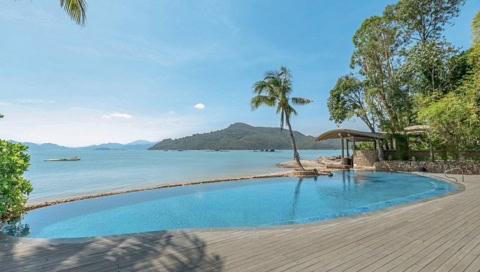 Infinity-Pool mit Holzterrasse direkt am Meer, umgeben von Palmen und Natur.