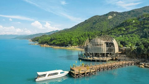 Bootssteg mit modernem Holzgebäude in ovaler Form über dem Wasser, dahinter grüne Hügel.