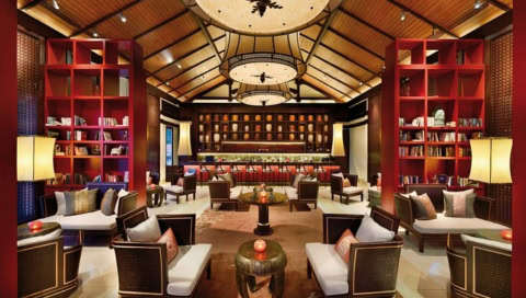 Elegante Hotelbar mit roten Regalen, gemütlichen Sesseln und stimmungsvoller Beleuchtung