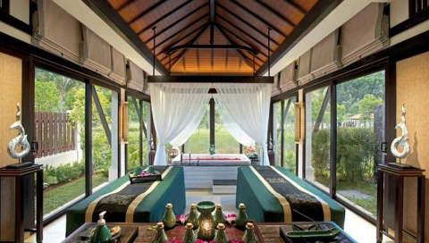 Blick in einen Spa-Behandlungsraum mit zwei Massageliegen, großen Fenstern und einer Badewanne im Hintergrund