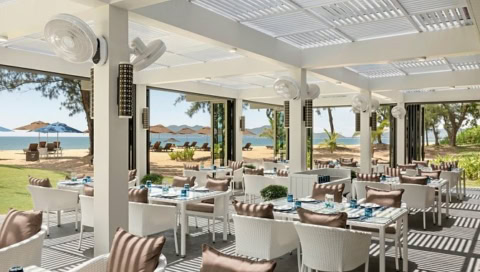 Offenes Strandrestaurant mit weißen Möbeln und Blick auf Meer und Sonnenschirme