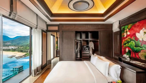 Schlafzimmer mit großem Bett, Holzmöbeln und Panoramafenster mit Blick auf den Strand