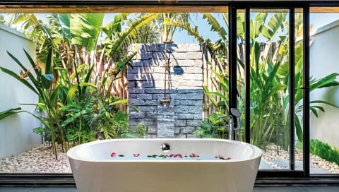 Freistehende Badewanne mit Blüten, Blick in tropischen Garten mit Außendusche