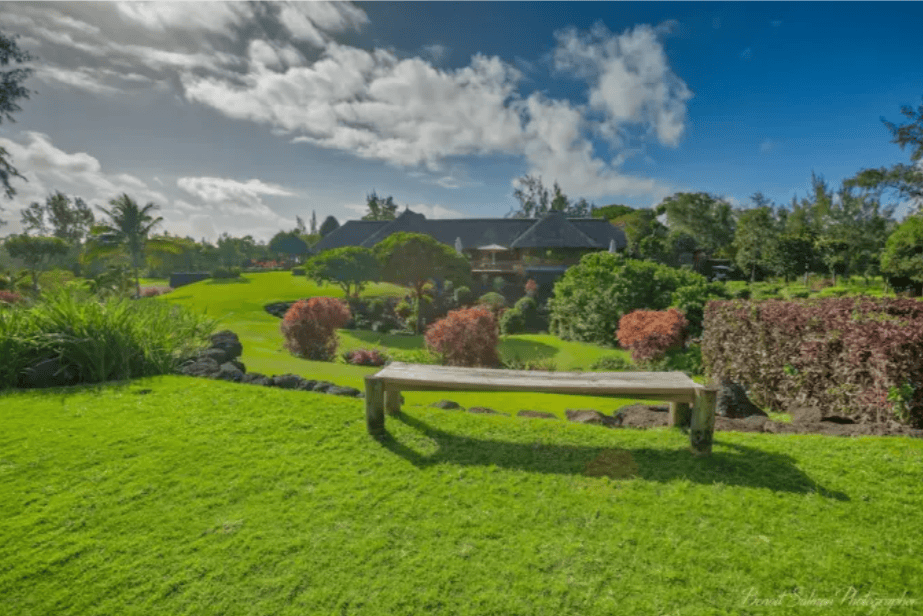 Panoramablick auf die weitläufige Gartenanlage mit einer Holzbank im Vordergrund und üppiger tropischer Vegetation