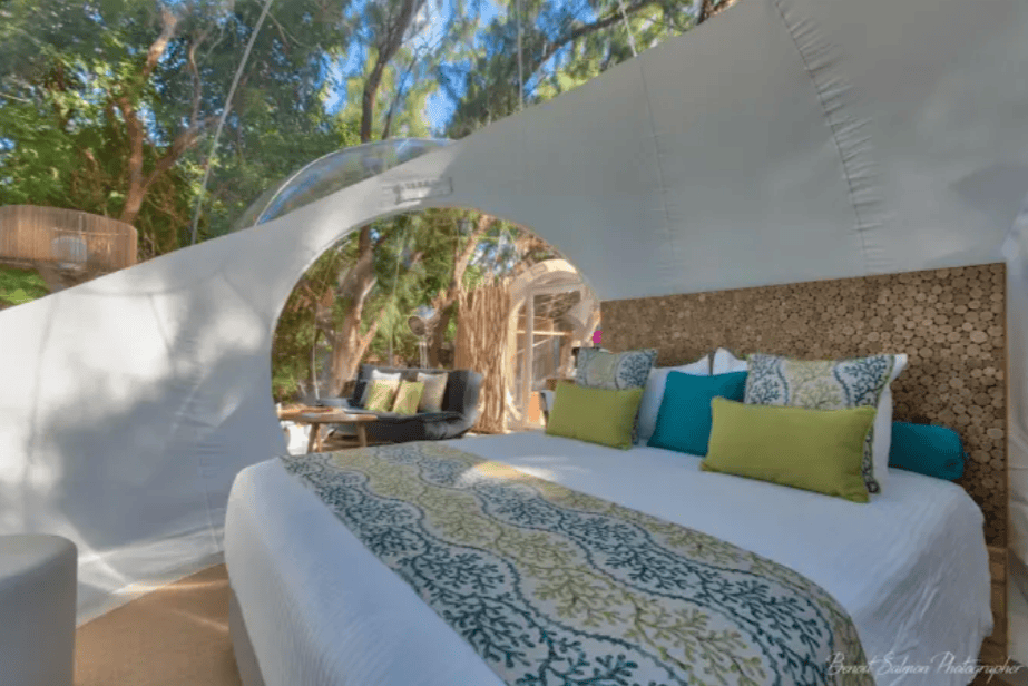 Helles Schlafzimmer mit großem Bett und transparentem Kuppeldach, umgeben von Natur