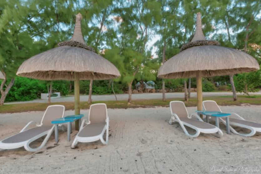 Zwei Liegen und zwei strohgedeckte Sonnenschirme am sandigen Strandbereich