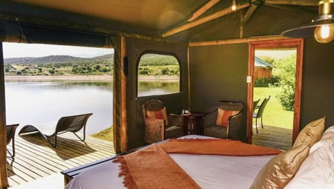 Zelt mit Doppelbett, zwei Sesseln und einer Veranda mit Ausblick über das Wasserloch