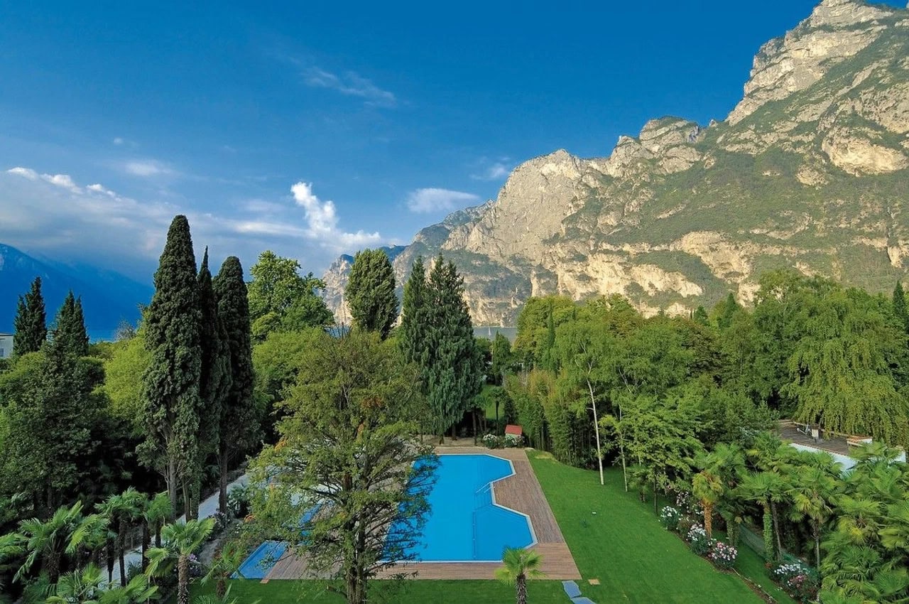 Poolbereich des Du Lac et Du Parc Grand Resort zwischen grüner Gartenanlage, hohen Bäumen und Felsenbergen