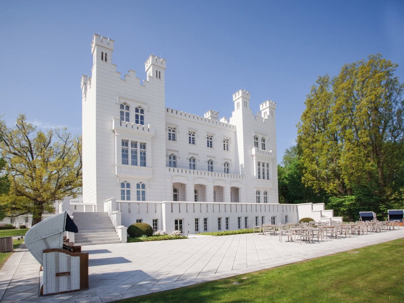 Helle Hotelfassade des Grand Hotel Heiligendamm mit großzügiger Terrasse, Außensitzplätzen, Strandkorb und gepflegtem Gartenbereich