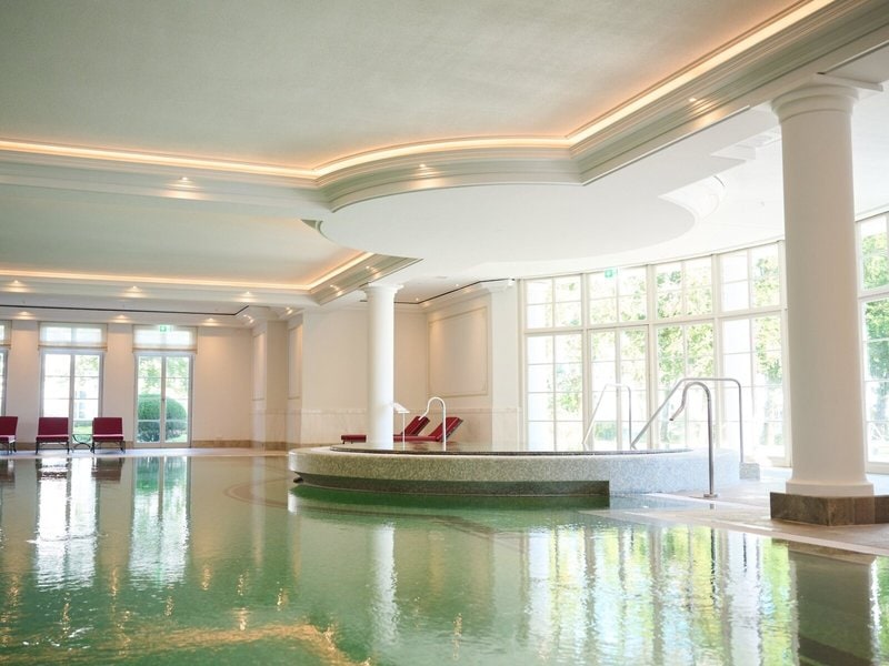 Eleganter Indoor-Pool im Grand Hotel Heiligendamm mit hellen Säulen, großem Whirlpool, Tageslichtfenstern und ruhiger Wellnessatmosphäre