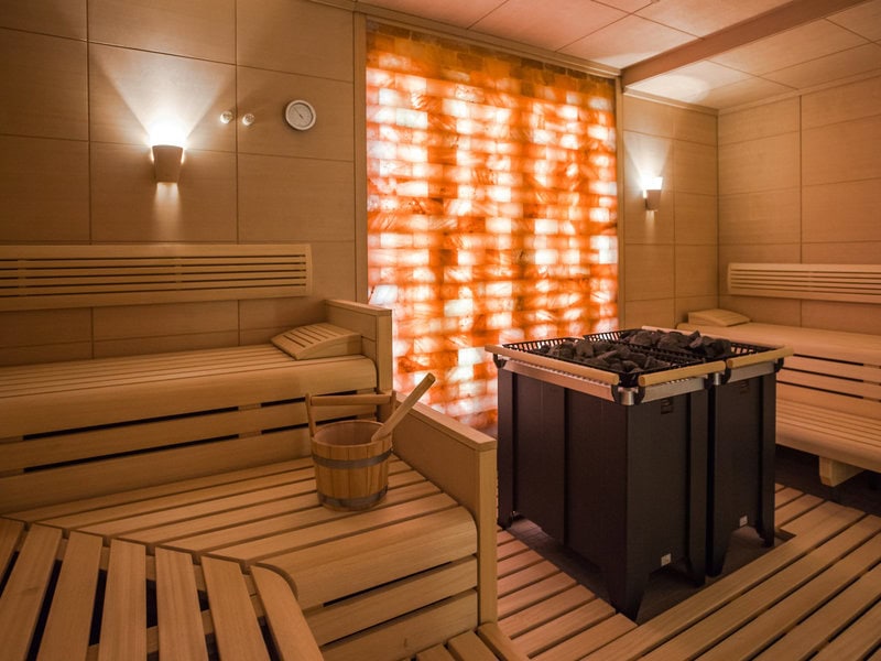 Warme Sauna im Grand Hotel Heiligendamm mit Holzbänken, Saunaofen, Holzeimer und leuchtender Salzwand im Wellnessbereich