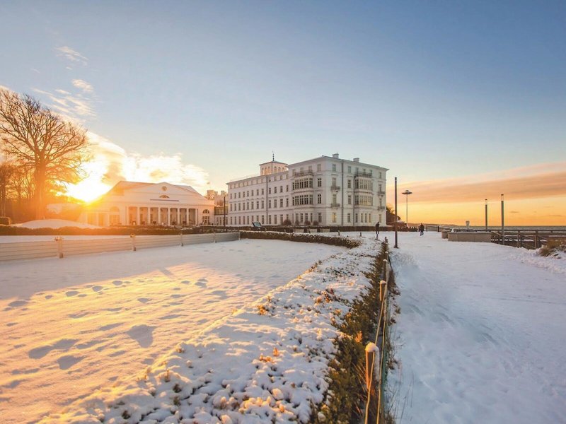 Grand Hotel Heiligendamm im Winter mit verschneiter Promenade, weißem Hotelgebäude, Ostsee im Hintergrund und warmem Sonnenuntergang