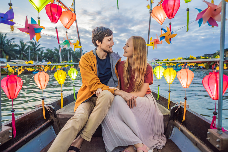 Romantisches Paar in einem Boot voller bunter Laternen auf dem Fluss in Hoi An am Abend.