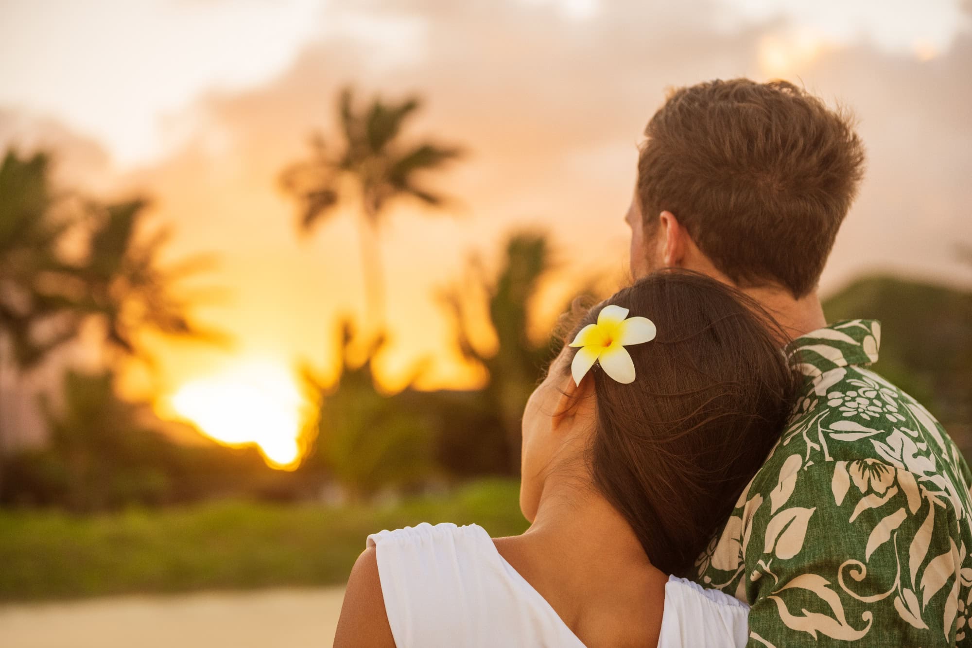 Romantisches Paar sitzt am Strand von Hawaii und blickt in einen goldenen Sonnenuntergang.