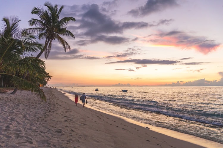 Paar läuft bei Sonnenuntergang am palmengesäumten Strand von Mauritius entlang