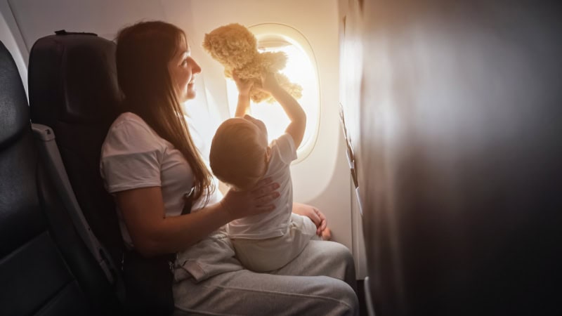 Eine Mutter mit Baby im Flugzeug. Das Baby hält einen Teddybär