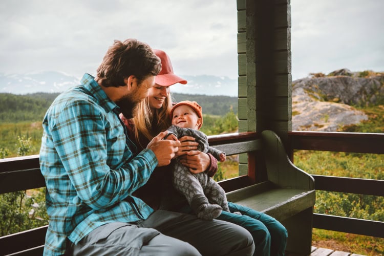 Eine Mutter und ein Vater sitzen mit ihrem Baby auf einer Bank im Gebirge