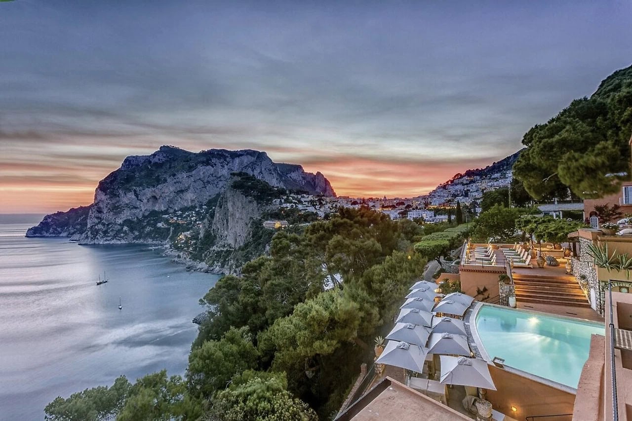 Blick vom Hotel Punta Tragara über Pool, Terrassen, Küste und Felsen von Capri bei Sonnenuntergang