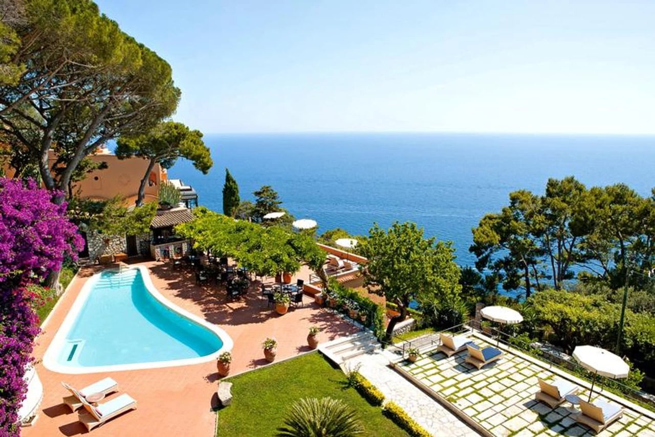 Poolbereich des Hotel Punta Tragara mit Sonnenliegen, mediterranen Pflanzen und weitem Blick auf das Meer