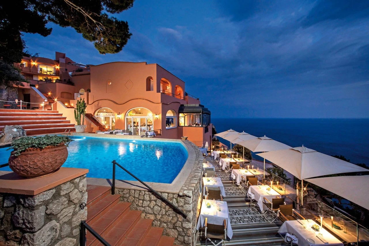 Abendlicher Pool- und Restaurantbereich im Hotel Punta Tragara mit gedeckten Tischen und Blick auf das Meer