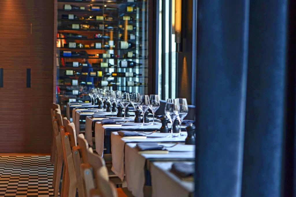 Gedeckte Restauranttische im Hôtel de Nell mit Weingläsern, Holzmöbeln und Weinregal im Hintergrund