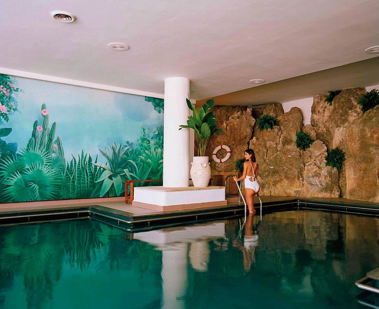 Indoor-Pool im Jumeirah Capri Palace mit türkisfarbenem Wasser, Felswand, tropischer Wandmalerei und ruhiger Spa-Atmosphäre