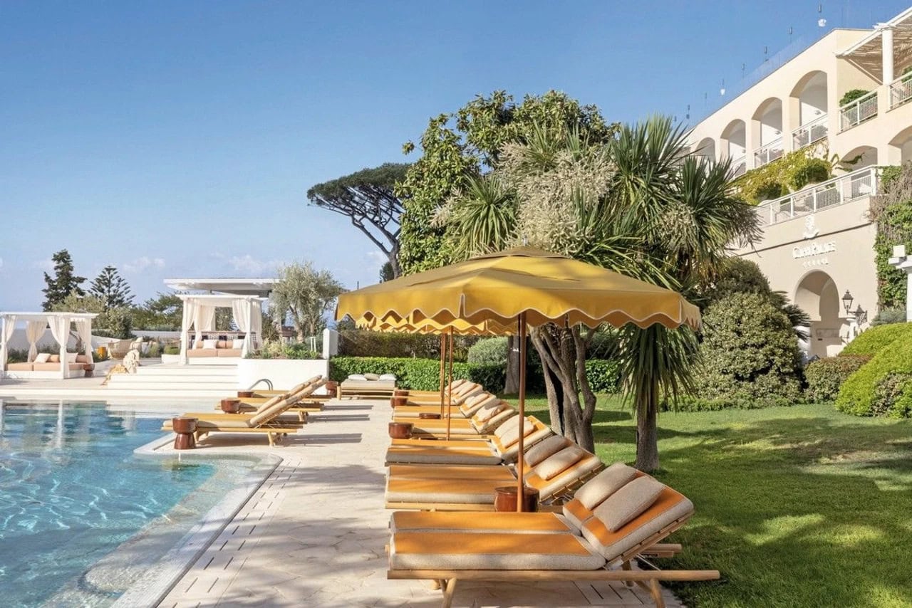 Poolbereich im Jumeirah Capri Palace mit gelben Sonnenliegen, Sonnenschirmen, mediterranen Pflanzen und Hotelgebäude