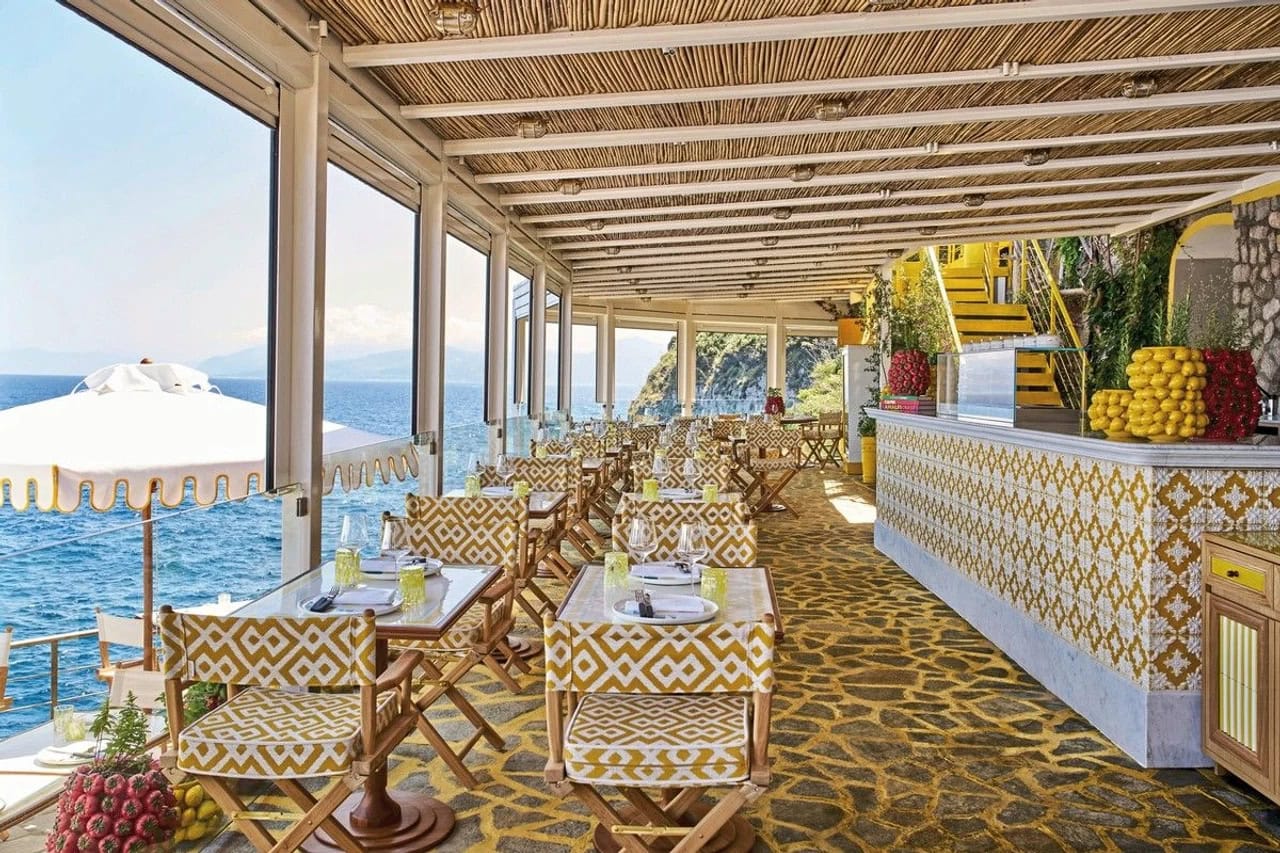 Restaurantterrasse im Jumeirah Capri Palace mit gedeckten Tischen, gelb gemusterten Stühlen und direktem Meerblick