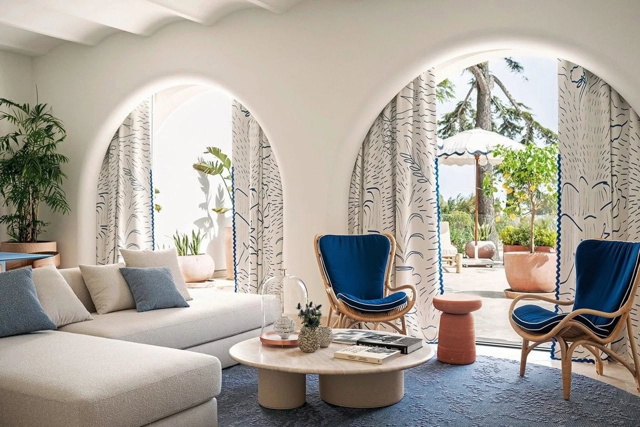 Heller Wohnbereich im Jumeirah Capri Palace mit Sofa, blauen Sesseln, Rundbogenfenstern und mediterraner Terrasse