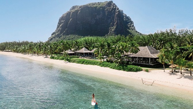 Strand von LUX Le Morne mit Blick auf den Berg Le Morne Brabant und einer Frau auf dem Paddleboard im klaren, türkisfarbenen Wasser