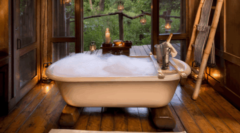 Freistehende Badewanne mit Schaum und Kerzenlicht, umgeben von Holz und Naturblick