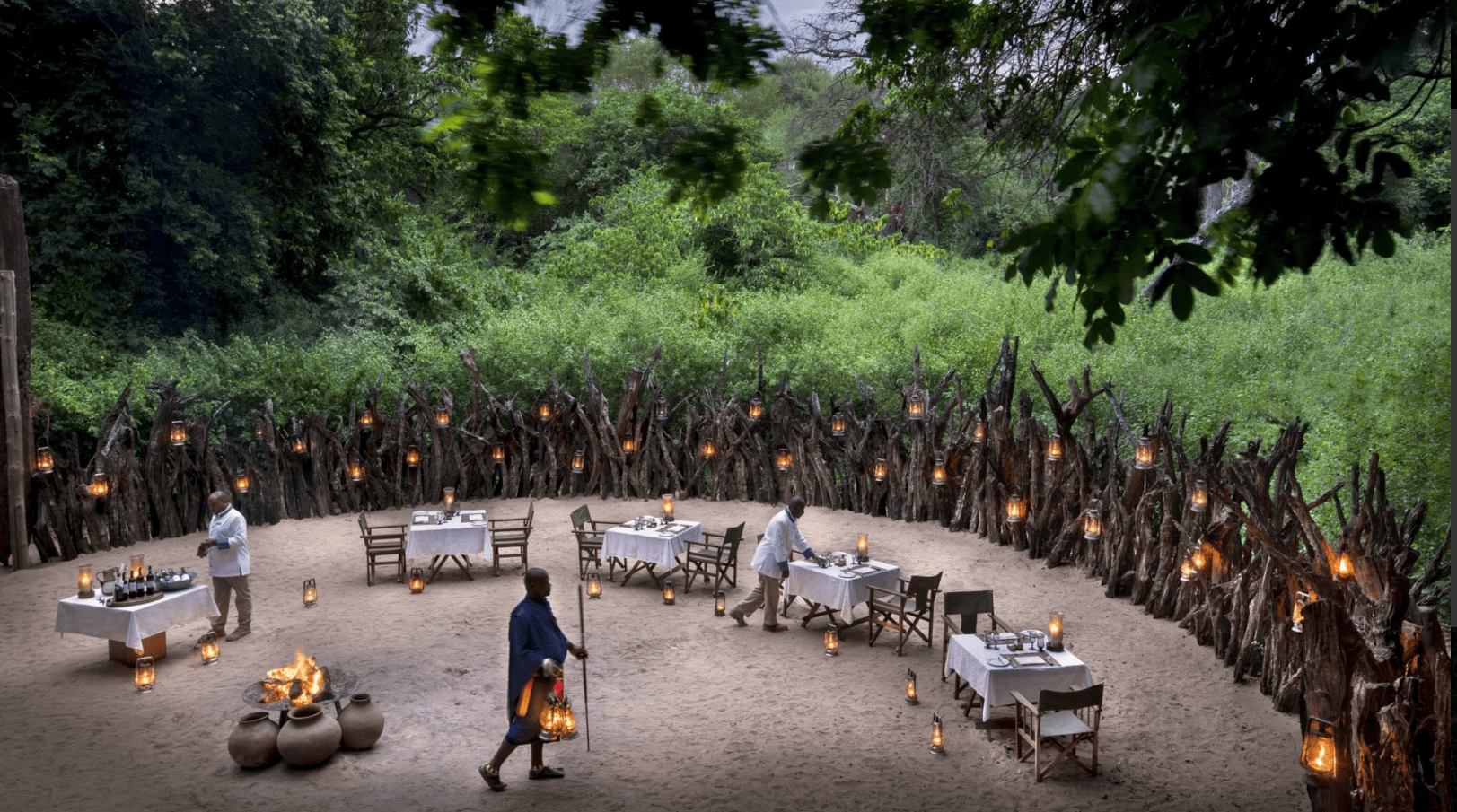 Offenes Restaurant unter Bäumen mit Lagerfeuer und Laternenbeleuchtung