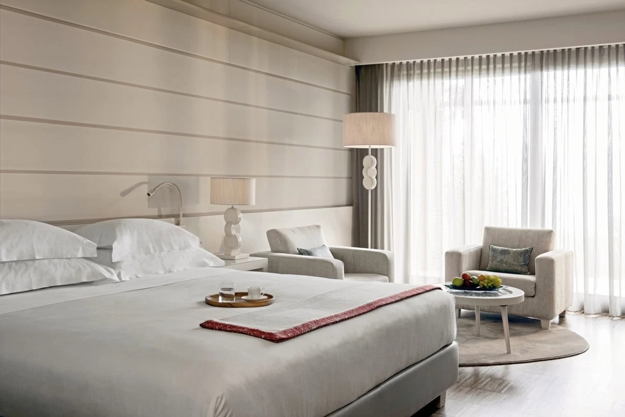 Helles Doppelzimmer im Lefay Resort & Spa Lago di Garda mit großem Bett, Sitzecke und bodentiefen Vorhängen
