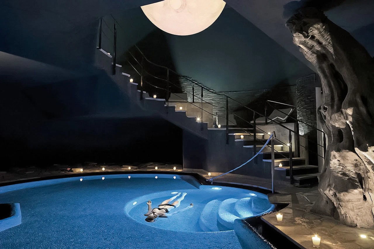 Stimmungsvoller Indoorpool im Lefay Resort & Spa Lago di Garda mit Kerzenlicht, Felswand und beleuchtetem Wasser