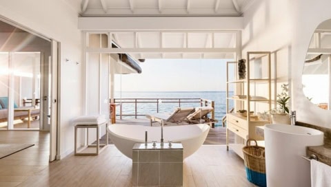 Badezimmer in einer Suite, die Glasfront lässt sich öffnen, sodass man von der Badewanne direkt auf das Meer schauen kann