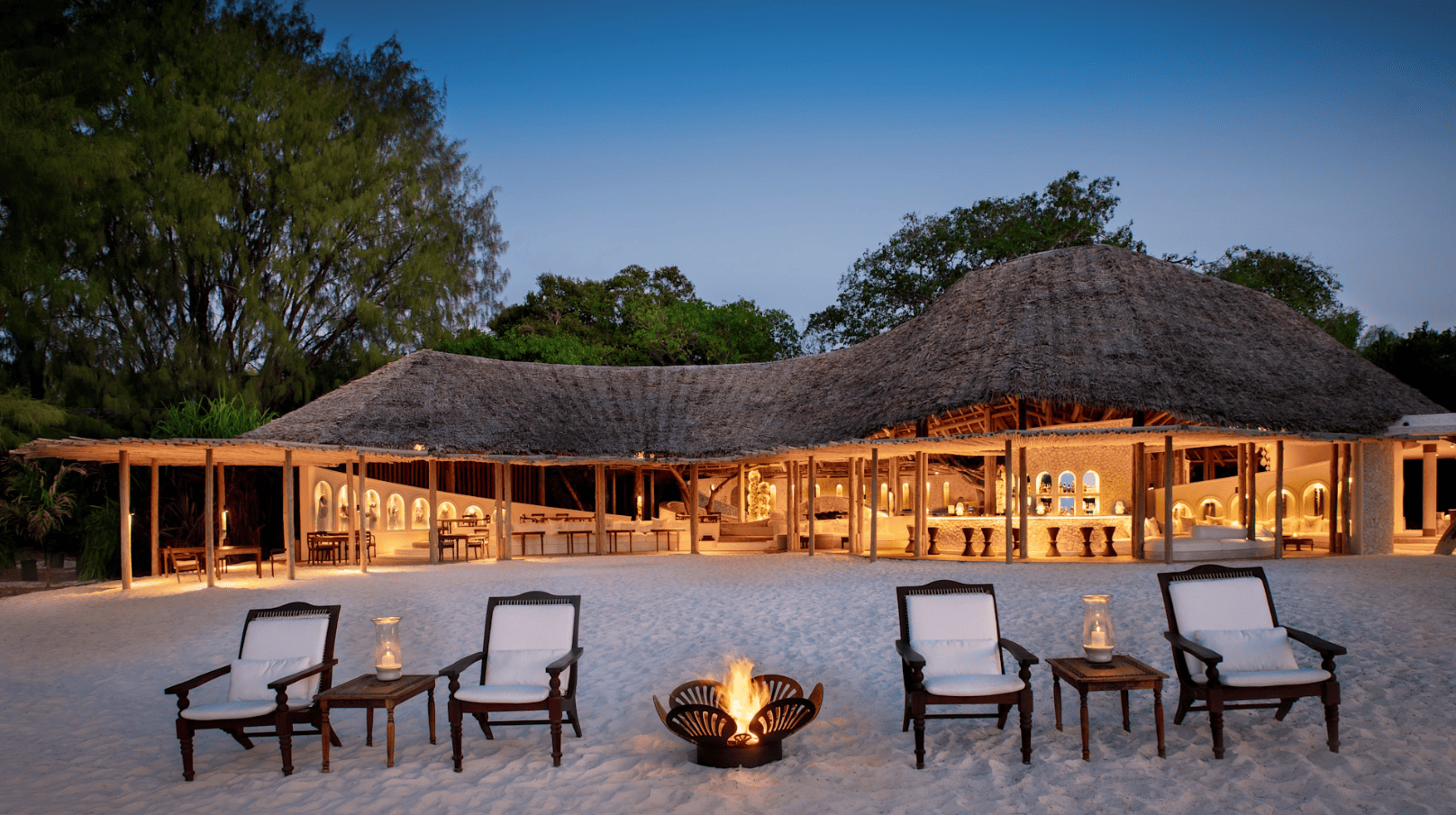 Außenbereich der Lodge direkt am Strand mit Feuerstelle und Liegestühlen im Sand