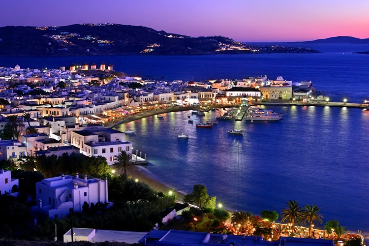 Abendaufnahme des beleuchteten Hafens von Mykonos-Stadt mit Blick auf die Bucht und das funkelnde Nachtleben.