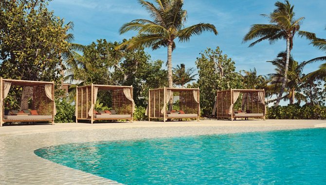 Sonnenliegen und private Cabanas am Poolbereich des Patina Maldives mit tropischer Vegetation und Palmen im Hintergrund
