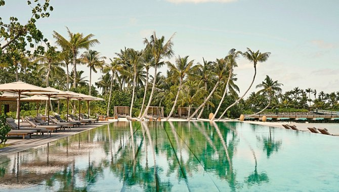 Infinity-Pool mit ruhiger Wasseroberfläche, Sonnenschirmen und Palmen im Patina Maldives Fari Islands