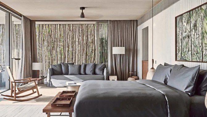 Schlafbereich der One Bedroom Beach Pool Villa mit großem Bett, Sitzsofa und bodentiefen Fenstern