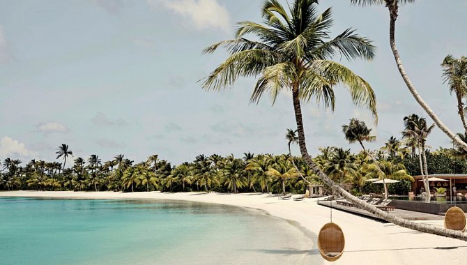 Weißer Sandstrand mit geschwungenen Palmen und ruhiger Lagune im Patina Maldives